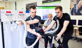 Sport, Fitness and Wellbeing Learner on exercise bike, being assisted by another Boston College Learner and Staff Member