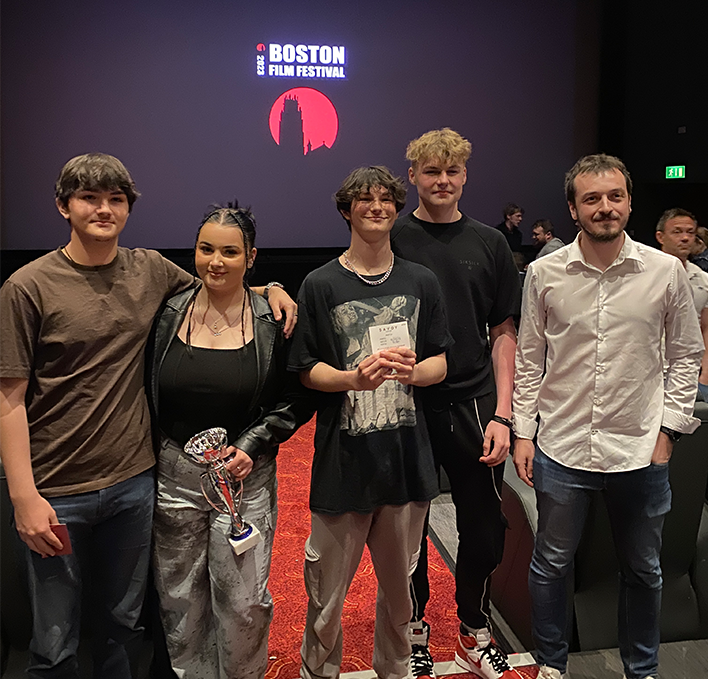 Learners and lecturer holding certificates and trophies in front of the cinema screen.