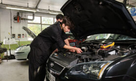 Boston College Automotive Technologies Learner working on the engine of the black car.