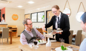 Boston College Catering and Hospitality Learner serving food to Eden Restaurant Customer