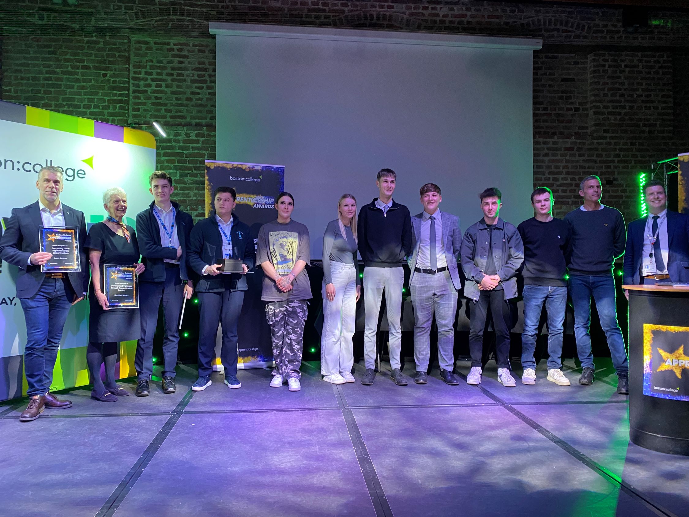 A photo of the winners at Boston College Apprenticeship Awards - a line up of 12 people standing on a stage holding certificates